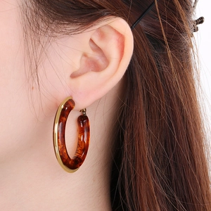 Close-up of a model wearing retro amber resin hoop earrings with golden metal edges