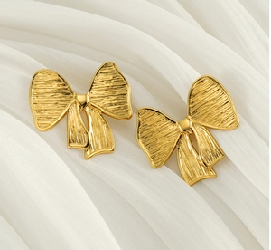 Gros plan de boucles d'oreilles nœud dorées avec texture brossée sur soie blanche