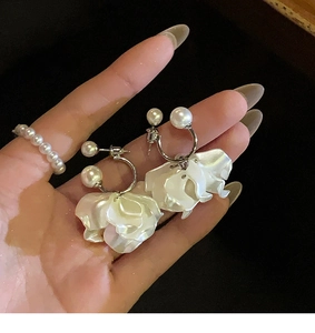 Dettaglio di eleganti orecchini a fiori bianchi con perle mostrati tenuti in mano