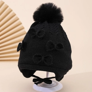 Detail of toddler black knit hat featuring faux fur pom-pom and bow with earflaps