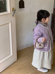 Détail de veste matelassée lavande à bordure florale et jupe beige sur un enfant
