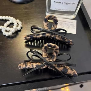 Elegant leopard print bow hair claw clip with black leather detail on dark tabletop