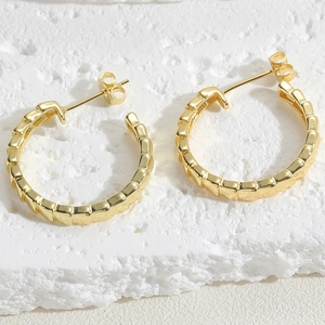 Detailed view of gold plated chain style hoop earrings on a textured white stone base
