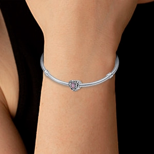 Detail of silver snake chain bracelet with heart-shaped bead and pink drop gem