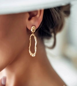 Close-up of asymmetric gold hammered oval earrings with baroque style on model's ear