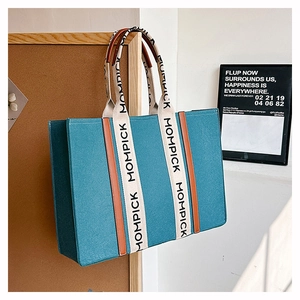 Detail of blue felt tote bag with contrast MOMPICK lettered straps and brown trim