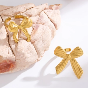 Detail of 18K gold plated bow rings showing polished and striped metal textures on a rock