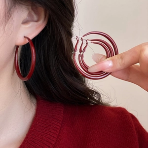 Macro detail of dark red enamel hoop earrings in various sizes worn by a model