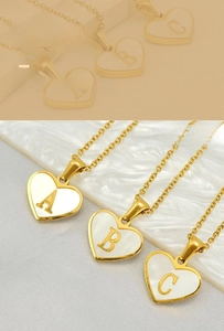 Close-up of heart-shaped gold necklace featuring white mother-of-pearl and letters