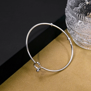 Detail of silver knot cuff bracelet featuring hollow heart charm and metallic beads