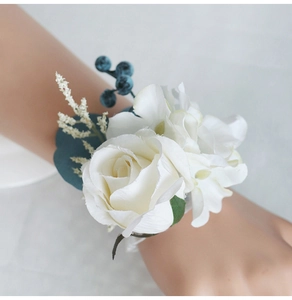 Detail of white silk rose wrist corsage with blue-green berries for wedding bridesmaids