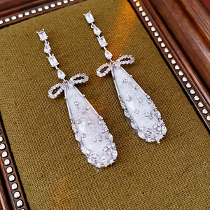 Detail of silver drop earrings with zircons and shell pendants on green velvet