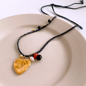 Détail macro du pendentif cœur doré sur collier en corde tressée avec perles