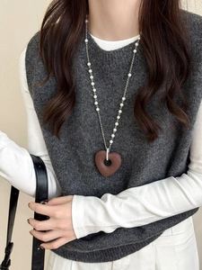 Detail of a brown heart pendant on a pearl chain necklace worn over a sweater