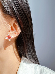 Close-up of red and white enamel flower earrings with gold-toned details on ear