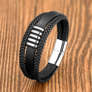Detail of multi-layer black braided leather bracelet with silver magnetic buckle on wood