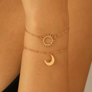Close-up of a double-layered gold bracelet featuring sun and crescent moon pendants on wrist
