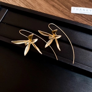 Detail of matte gold orchid flower earrings with textured petals on a black tray