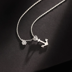 Macro detail of silver anchor and helm pendants on a high-end minimalist nautical necklace