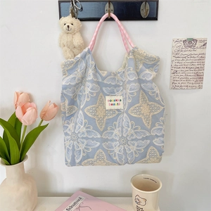 Détail de broderie papillon en dentelle blanche sur un sac fourre-tout bleu clair et rose