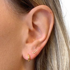 Close-up of golden cluster stud earrings with white marquise crystals on a model's ear