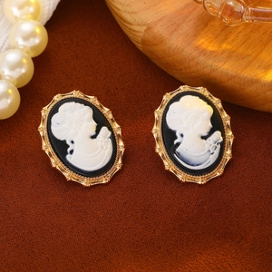Close-up of vintage cameo earrings with white female profile relief on black background