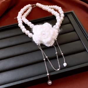 Close-up of double-layer pearl necklace featuring a white knit flower and silver tassels