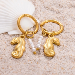Boucles d'oreilles créoles hippocampe dorées avec perles blanches sur du sable