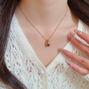 Close-up of gold-plated lucky bag necklace with red and green stones on a model