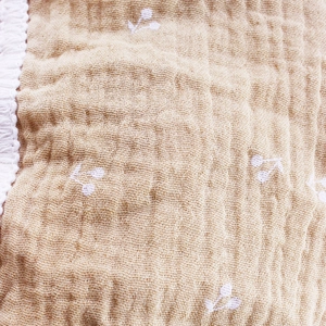 Close-up of muslin baby blanket with white cherry print and elegant lace trim detail
