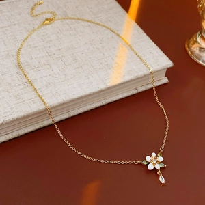 Dettaglio di una collana dorata con fiori smaltati bianchi e un cristallo a goccia