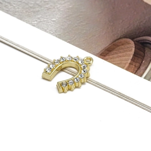 Macro detail of a golden horseshoe pendant set with multiple white sparkling zircons