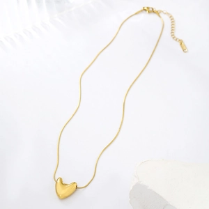 Minimalist gold heart pendant necklace with sleek snake chain on white stone display