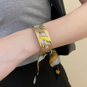 Detail of a hammered gold open cuff bracelet with an elegant wrapped patterned silk scarf