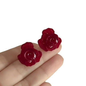 Dopamin-Ohrstecker mit mehrlagigen dunkelroten Rosenblüten zwischen den Fingern