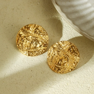 Detail of gold titanium steel earrings with textured hammered finish on stone surface
