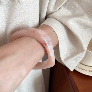 Macro detail of wide resin bangle featuring a soft pink marble texture on the wrist