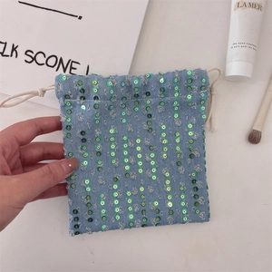 Detailed view of light blue denim drawstring pouch with green sequins and frayed edges