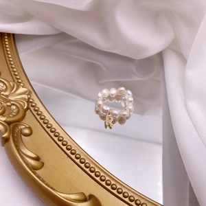 Detail of French vintage pearl ring with a gold letter R charm on a mirror surface