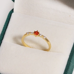 Macro shot of gold ring with six-prong set orange-red gem and side white zircon stones