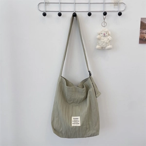 Detail of green pleated canvas tote bag with a cute lamb charm on a minimalist wall hook