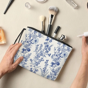 Blue floral cosmetic bag with black zipper and wrist strap on a vanity counter
