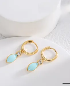 Detailed close-up of gold brass earrings with blue enamel leaf and zircon crystal on a stand