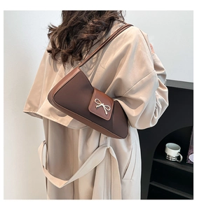 Brown leather baguette bag with silver bow detail shown on a model in a trench coat