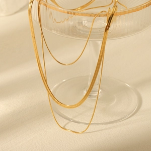 Three-layer 18K gold plated stainless steel layered necklace on a glass cup