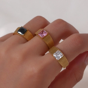 Three gold rings with emerald-cut black, pink, and white gemstones on model fingers