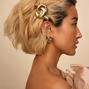 Nahaufnahme eines Models mit goldenen gedrehten Knotenohrringen und Haarklammer