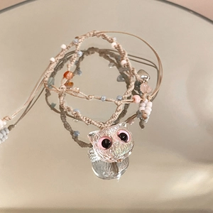 Macro detail of hand-woven owl pendant with pink eyes and colorful beads on mirror