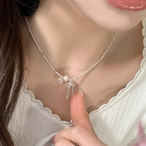Detail of silver necklace with bow pendant, pearl and pink heart on female model