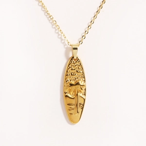 Detailed view of golden palm tree relief on a surfboard pendant necklace with fine chain